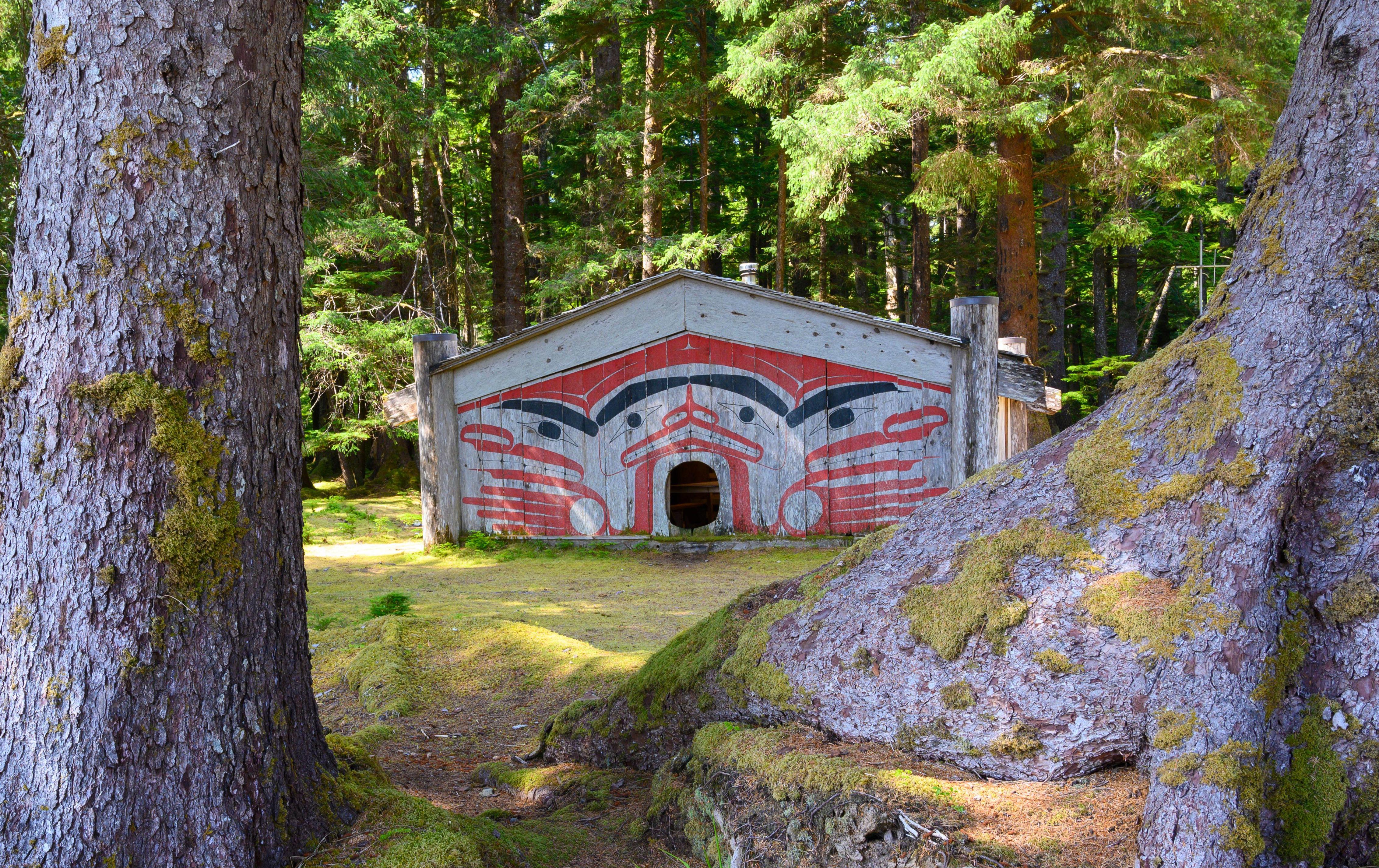 A Haida Gwaii house with painted faces, nestled in a mossy forest.