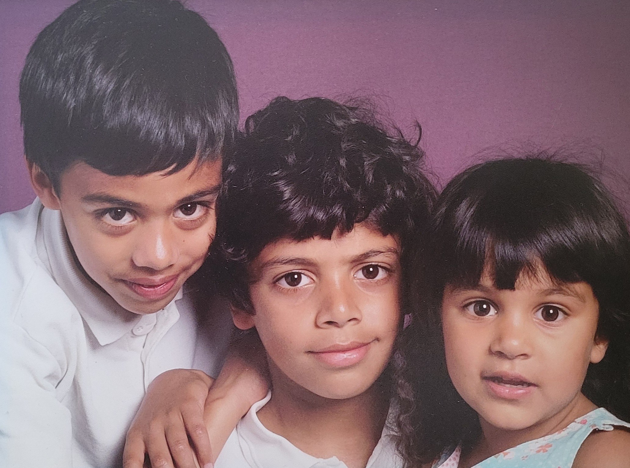School photo of three siblings; Omar (age 9) is in the middle.