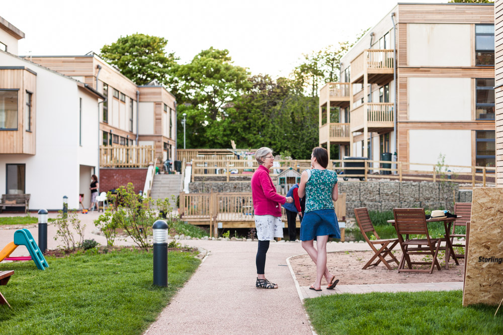 Two women conversing in the courtyard of a modern apartment building.
